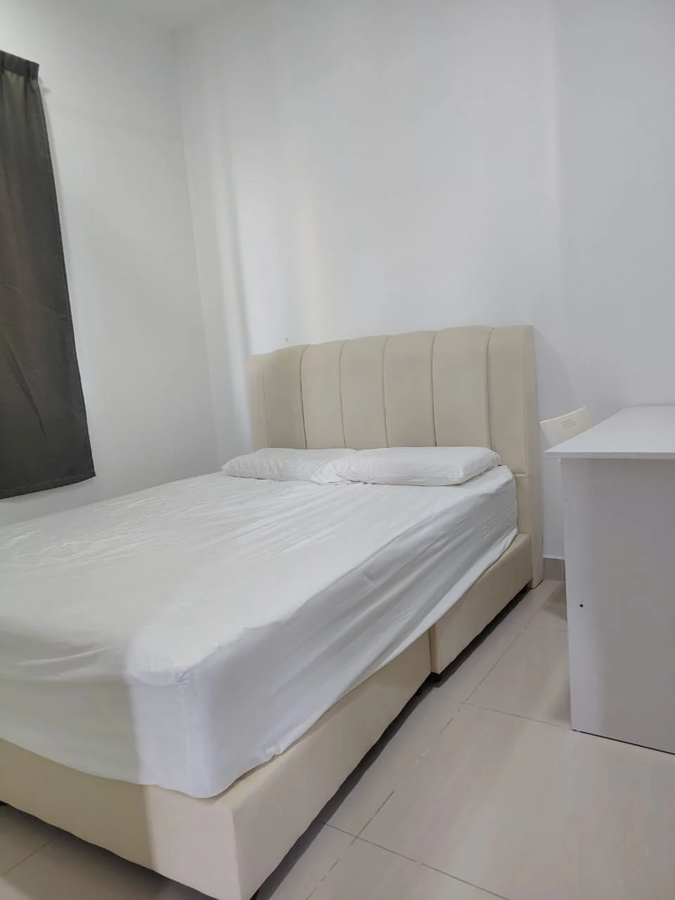 Bedroom features: queen-size bed, upholstered headboard, white bedding, light-coloured bed frame, white walls, grey curtains, tile flooring, nightstand, desk, window; style: modern.
